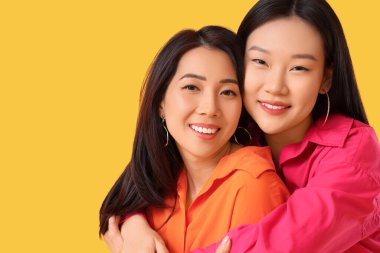 Güzel, genç, mutlu Asyalı kızlar şık kıyafetler içinde sarı arka planda sarılıyorlar.