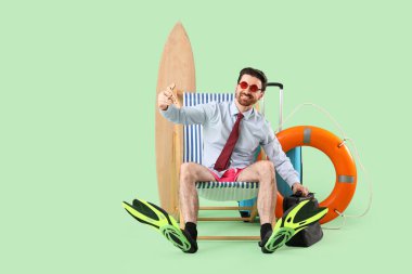 Ahşap uçakla ve yeşil arka planda iskemlede evrak çantasıyla genç bir işadamı. Yaz tatili kavramı