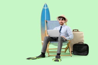 Yeşil arka planda dizüstü bilgisayarı olan genç bir iş adamı. Yaz tatili kavramı