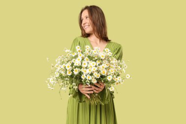 Yeşil arka planda bir buket papatya çiçeğiyle mutlu genç bir kadın.