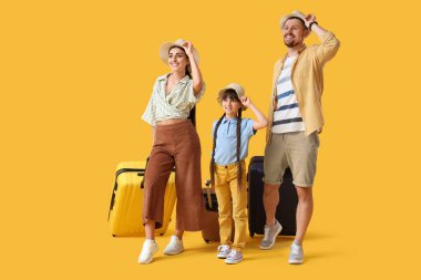 Sarı arka planda yürüyen bavullu turist ailesi.