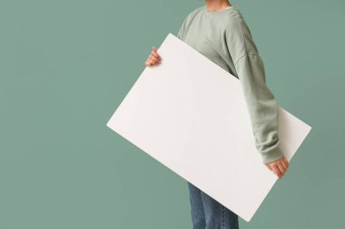 Yeşil arka planda boş poster tutan genç bir kadın.