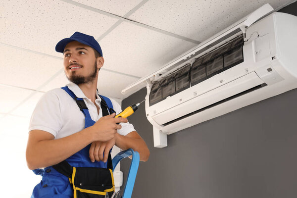 Male technician fixing air conditioner in room