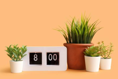 Turuncu zemin üzerinde saati olan yapay bitkiler.