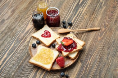 Lezzetli tost tabağı, farklı reçel kavanozları ve kahverengi ahşap arka planda böğürtlen.