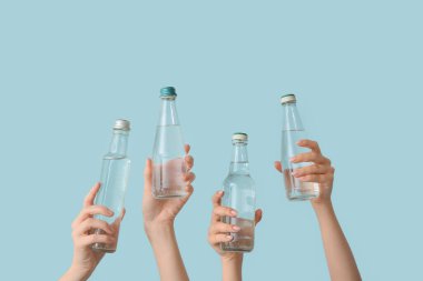 Mavi arka planda soğuk su şişeleri olan kadın eller.