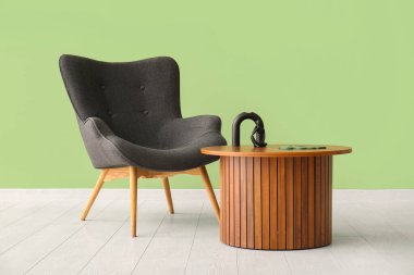 Gri koltuk ve yeşil duvarın yanındaki dekorlu ahşap sehpa.