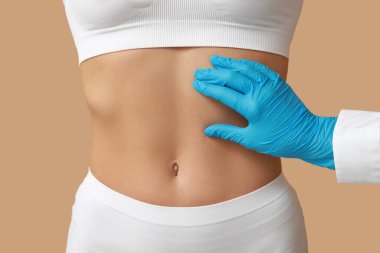 Düz göbekli genç bir kadın ve bej arka planda plastik cerrah, yakın plan.