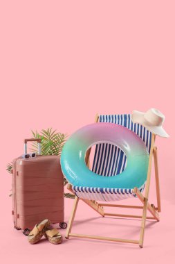 Güverte sandalyeli bavul ve pembe arka planda plaj aksesuarları.