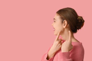 Güzel genç bir kadın pembe arka planda işitme cihazına işaret ediyor.