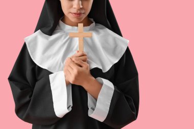 Pembe arka planda haç çizen genç rahibe