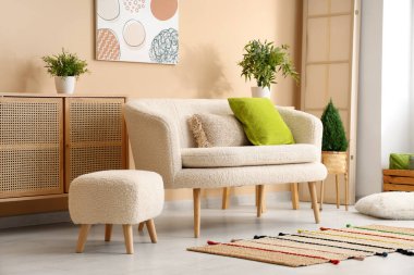 Bej duvarın yanında çekmeceleri ve kanepesi olan rahat bir oturma odası.