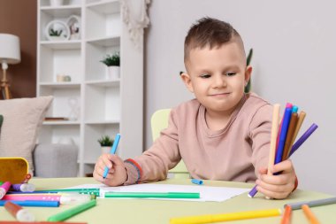 Masada keçeli kalemlerle çizen komik küçük çocuk.