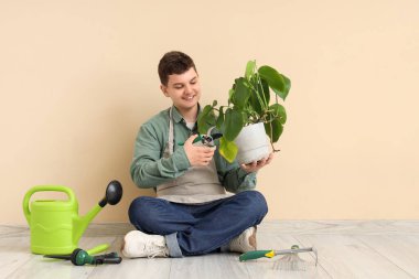 Bej duvarın yanında oturan bitkileri ve aletleri olan genç bahçıvan