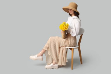 Gri arka planda, sandalyede oturan güzel narsisli çiçeklerle dolu güzel, genç ve mutlu bir kadın.