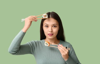 Güzel bir Asyalı kadın elinde lezzetli suşilerle yeşil arka planda çubuklar tutuyor.