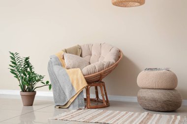 Aydınlık oturma odasının içinde koltuk, bitki ve puf var.