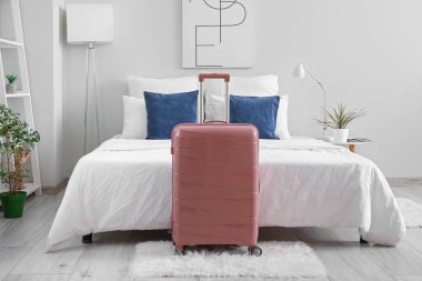 Yatağın yanında bavulu olan hafif bir otel odası.