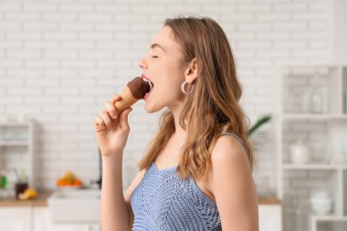 Evde waffle külahında çikolatalı dondurma yiyen genç bir kadın.