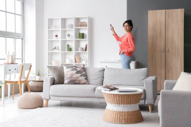 Gülümseyen genç Afro-Amerikalı kadın evdeki klimayı açıyor.