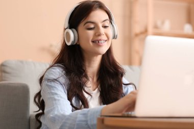 Oturma odasında kulaklıklı laptop kullanan genç bir kadın.