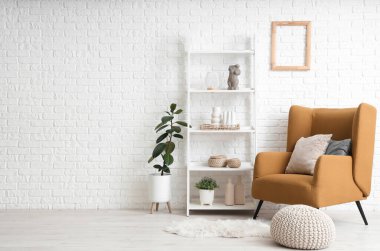 Beyaz tuğla duvarın yanında rahat koltuğu ve raf ünitesi olan modern bir oda.