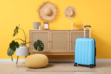 Oturma odasının içindeki sarı duvarın yanında bavul ve sandık dolusu çekmece var.