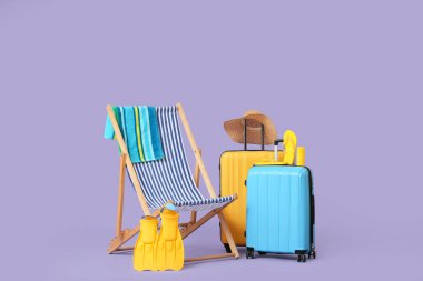 Çizgili iskemle, bavullar ve eflatun arka planda plaj aksesuarları.