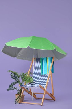 Çizgili güverte sandalyesi, ev bitkisi, havlu ve şemsiye eflatun arka planda