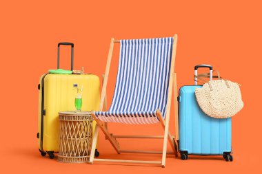 Çizgili iskemle, bavullar ve portakal rengi arka planda bir bardak kokteyl.