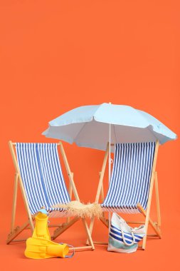 Çizgili iskemle, şemsiye ve turuncu arka planda plaj aksesuarları.