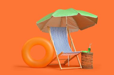 Çizgili iskemle, şemsiye, şişirilebilir yüzük ve turuncu arka planda bir bardak kokteyl.