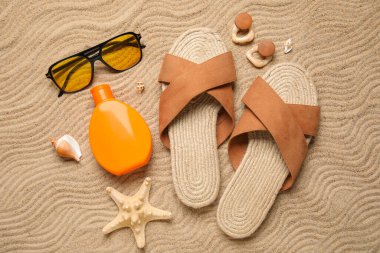 Bir şişe güneş kremi, deniz kabukları ve kumsal aksesuarları arka planda, yakın plan.