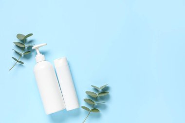 Duş jeli şişeleri ve mavi arka planda okaliptüs dalları olan kompozisyon