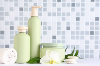 Duş jeli şişeleri, spa taşları ve havluyla mavi fayans duvarının yanındaki masada, yakın plan.