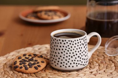 Bir fincan sıcak kahve ve ahşap masada tatlı kurabiyeler.