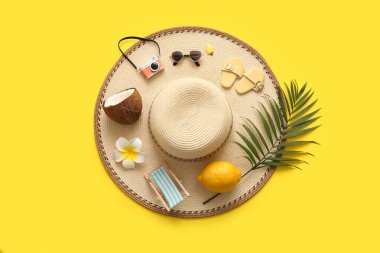 Sarı arka planda hindistan cevizi, limon ve plaj aksesuarlarıyla yaz kompozisyonu
