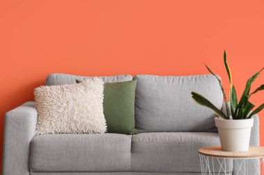 Oturma odasındaki turuncu duvarın yanındaki masada rahat bir kanepe ve çiçek var.