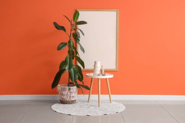 Odanın içindeki turuncu duvarın yanındaki masa ve bitki örtüsü.