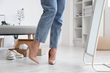 Genç bir kadın yeni bej rengi yüksek topuklu ayakkabılar deniyor. Aynanın yanında.