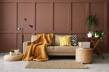 Kahverengi duvarın yanında rahat kanepe, masa ve dizüstü bilgisayarı olan bir oturma odası.