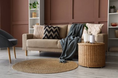 Oturma odasının içinde rahat bir kanepe ve kahverengi duvarın yanında bir masa var.