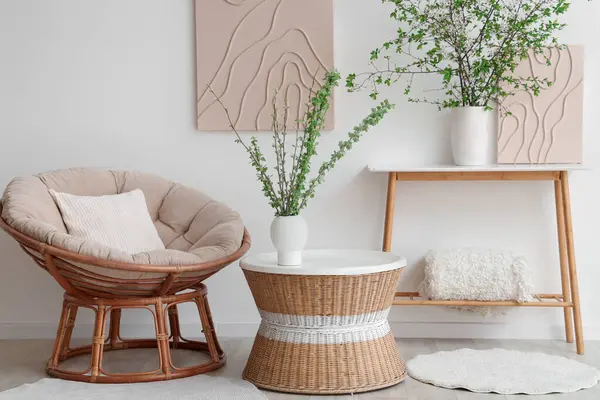 Rahat koltuk, kahve masası ve aydınlık oturma odasında çiçek açan dalları olan vazolar.