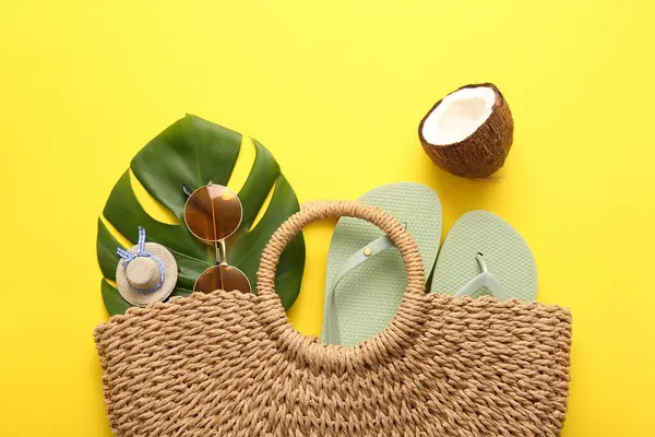 Sarı arka planda hasır çantalı, hindistan cevizi ve plaj aksesuarlı yaz kompozisyonu, yakın plan.