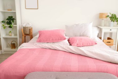 Yumuşak yastıklı rahat yatak ve açık renkli yatak odasında pembe battaniye.