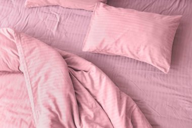 Yumuşak yastıklı rahat yatak ve buruşuk pembe yorgan, üst manzara.