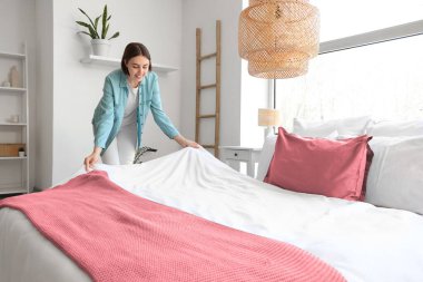 Genç bir kadın hafif yatak odasında yatak yapıyor.