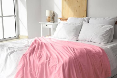 Yumuşak yastıklı rahat bir yatak ve açık yatak odasındaki pencerenin yanında pembe bir battaniye