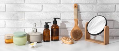 Farklı kozmetik ürünleri, ayna ve masaj fırçaları hafif tuğla duvarın yanındaki masada.