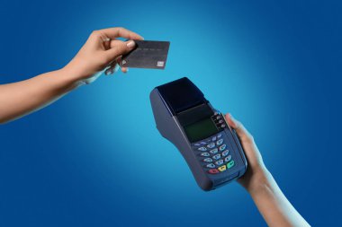 Kredi kartı olan bir kadın, mavi arka planda terminal üzerinden ödeme yapıyor.